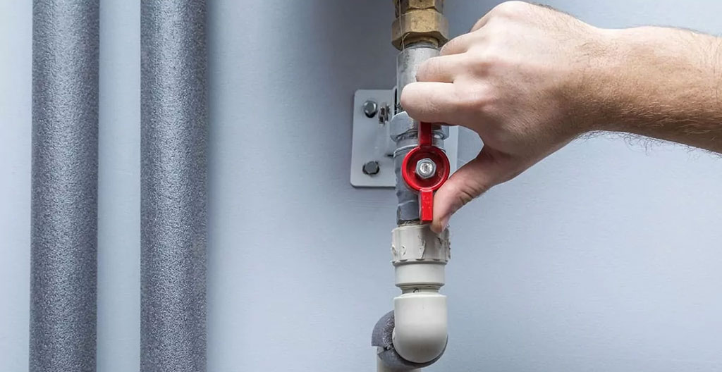 Plan rapproché d'une main adulte tournant une valve d'arrêt chromée sous un évier de cuisine contemporain