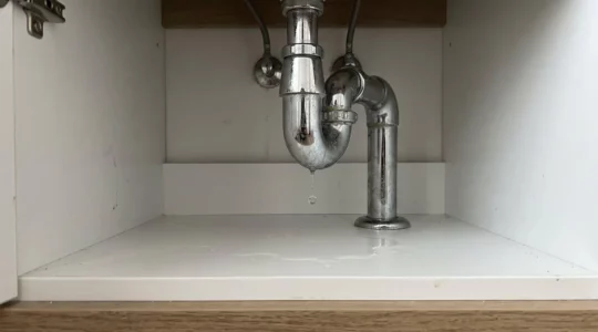 Gros plan sur des gouttes d'eau tombant d'un raccord chromé sous un lavabo contemporain dans une salle de bain lumineuse